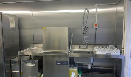 This image shows a ware-washing set up for a commercial kitchen. Including a pass through dishwasher and a glasswasher.