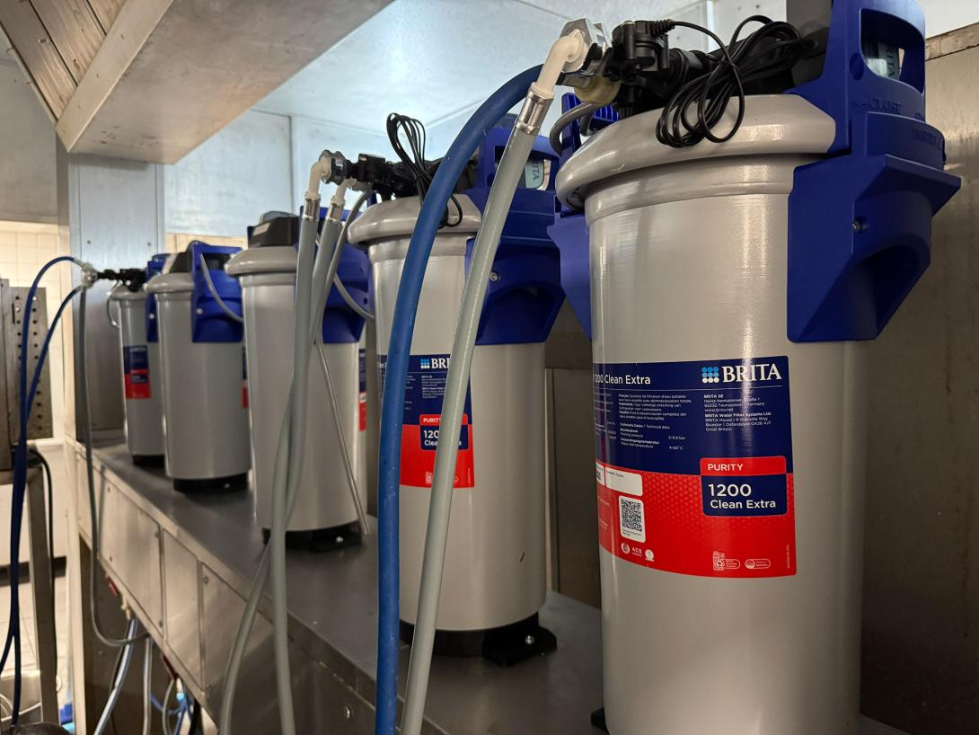 The image shows a section of a commercial kitchen installation featuring multiple BRITA Purity 1200 Clean Extra water filtration units connected by blue and grey hoses.