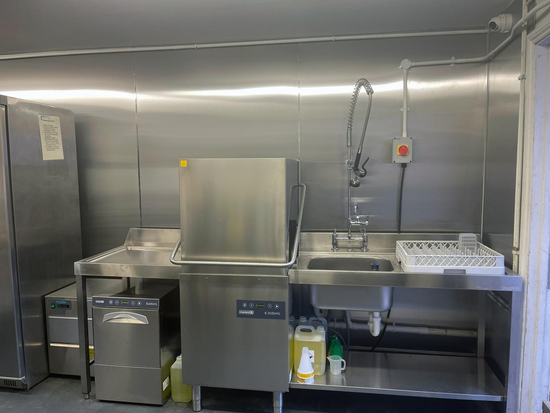 This image shows a ware-washing set up for a commercial kitchen. Including a pass through dishwasher and a glasswasher.